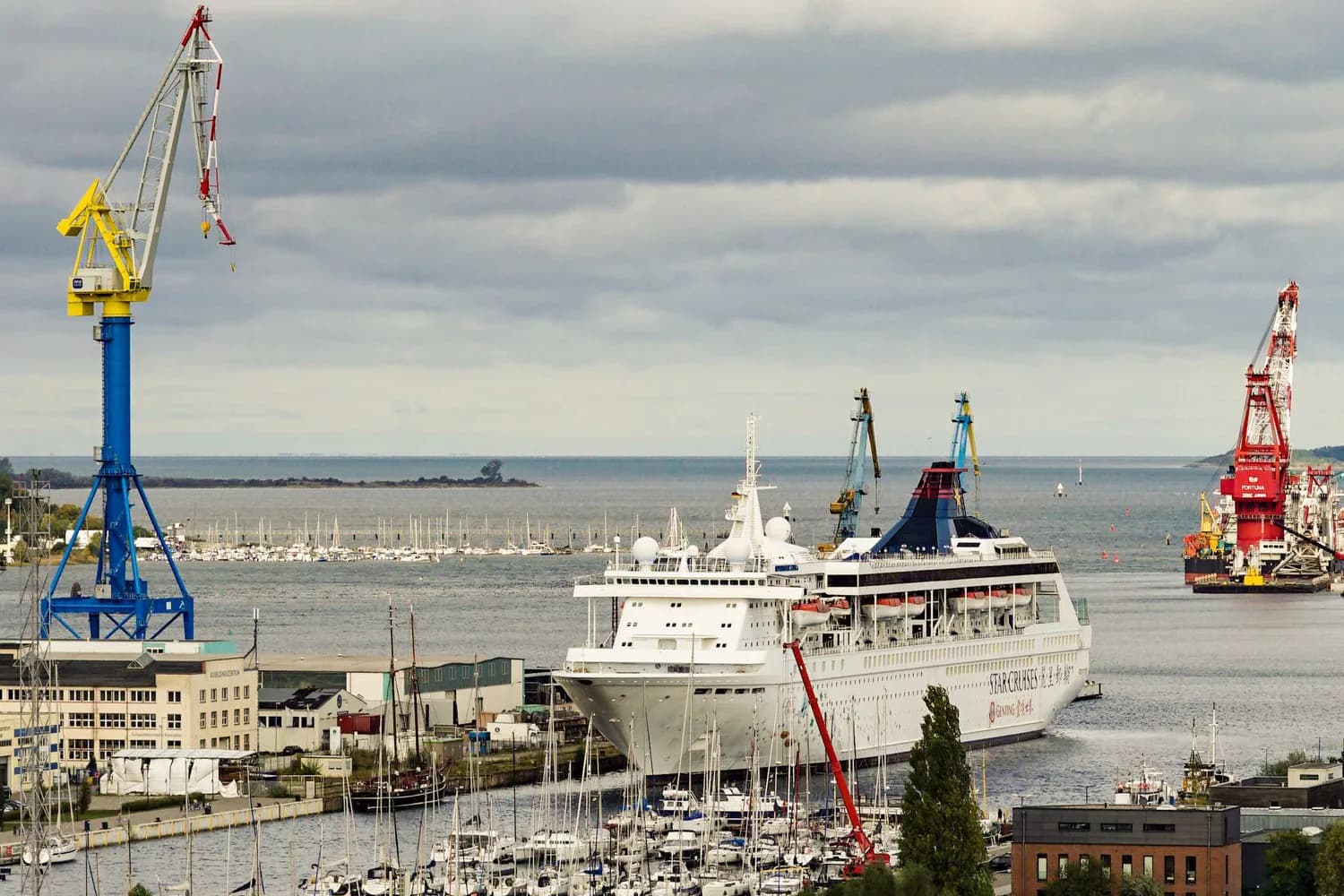 Kreuzfahrschiff am Kieler Hafen mit Hafenkränen und Jachthafen im Vordergrund