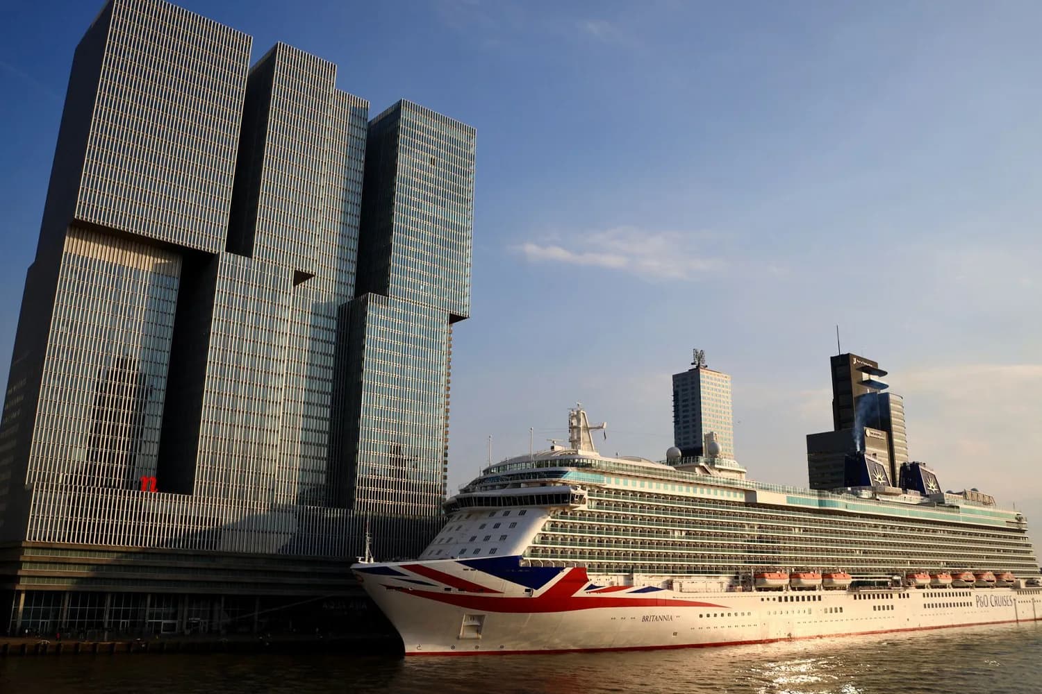 Kreuzfahrtschiff vor modernen Bürotürmen am Wasser in Rotterdam