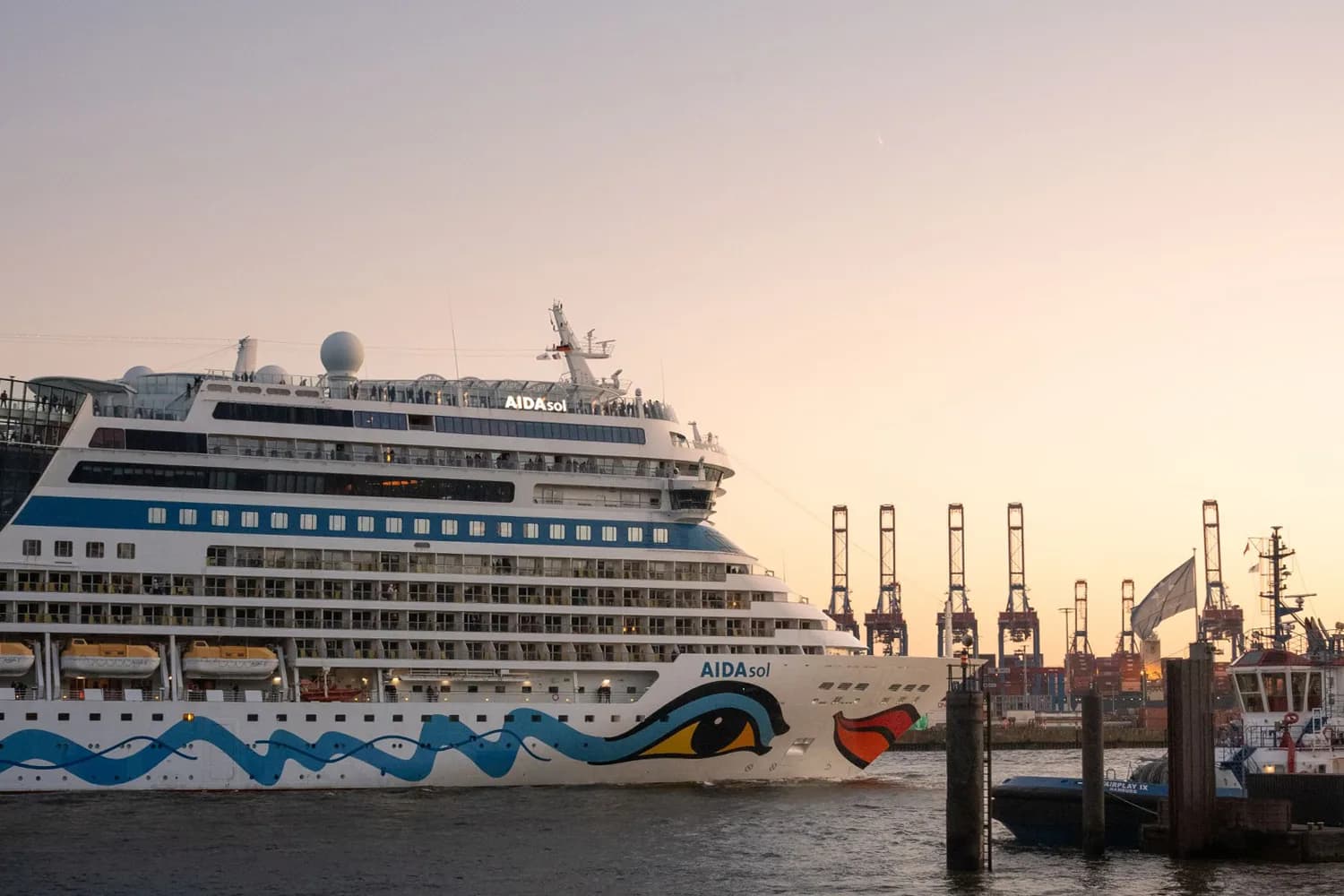 Kreuzfahrtschiff AIDAsol mit blauem Wellendekor am Bug im Hamburger Hafen mit Containerkränen im Hintergrund