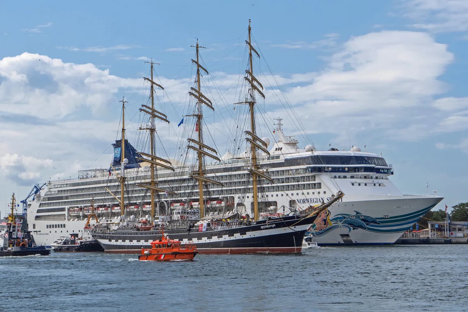 Segelschiff und Kreuzfahrtschiff im Hafen Rostock bei blauem Himmel mit weißen Wolken