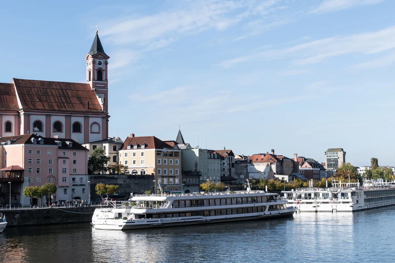 Flusskreuzfahrtschiff an der Uferpromenade von Passau mit historischer Altstadt und Kirchturm im Hintergrund