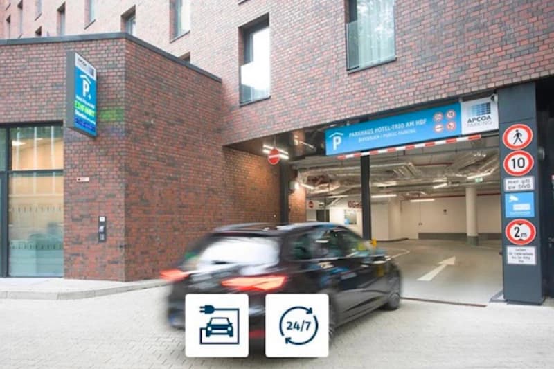 Einfahrt zur Tiefgarage in Backsteinbau, ein Auto fährt ins beleuchtete Parkportal, Verkehrsschilder am Eingang sichtbar.