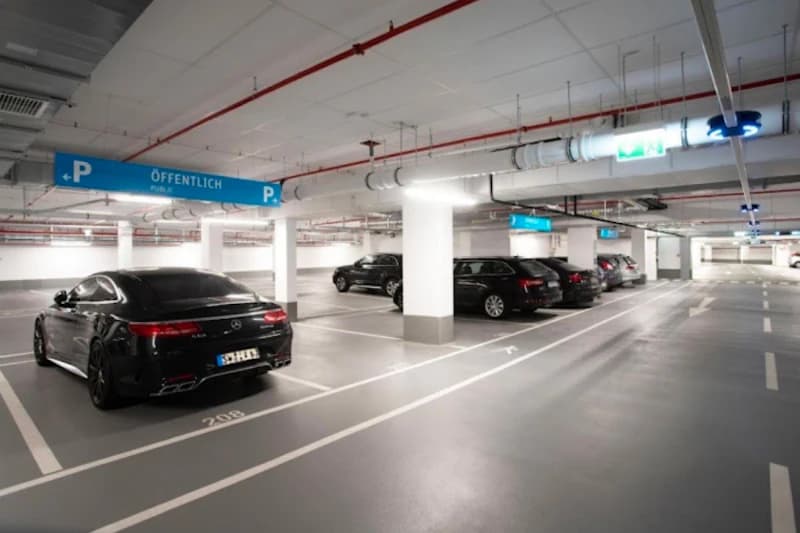 Helle Tiefgarage mit abgestellten Autos, Säulen, weißen Parkmarkierungen und blauen Schildern ÖFFENTLICH.