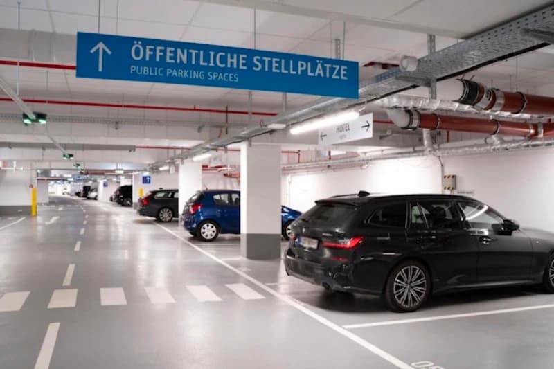 Tiefgarage mit mehreren geparkten Autos, blaues Schild ÖFFENTLICHE STELLPLÄTZE und markierten Fahrspuren.