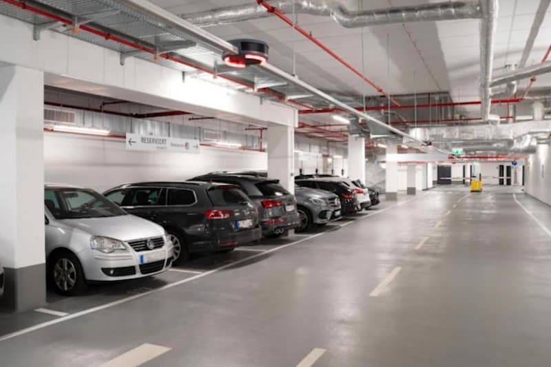 Innenraum einer beleuchteten Tiefgarage mit nebeneinander geparkten Autos an linken Stellplätzen und freier Fahrspur rechts.