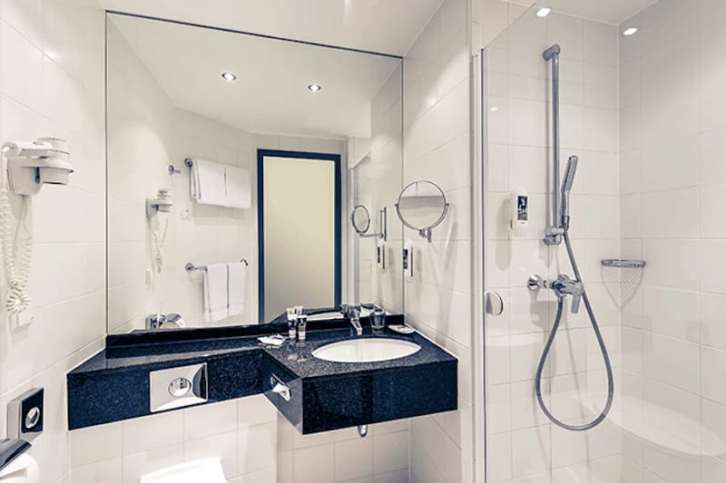 Kompaktes Badezimmer mit schwarzer Waschablage, Waschbecken, großem Spiegel und Dusche mit Glasabtrennung.