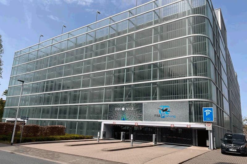Mehrstöckiges Parkhaus mit transparenter Fassade, Einfahrten im Erdgeschoss und Schild FRA Parking am Eingang.