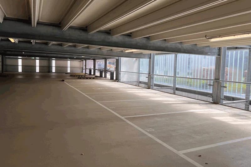Leeres Parkdeck im Parkhaus mit markierten Stellplätzen, Stahlträgern und seitlichen Lichtöffnungen.
