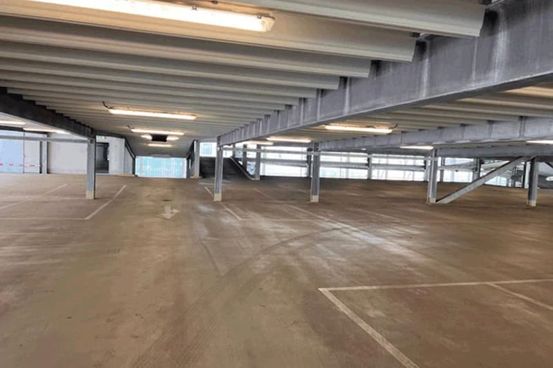 Leere Ebene eines mehrgeschossigen Parkhauses mit Bodenmarkierungen, Pfeil, Stützen und sichtbaren Deckenbalken.