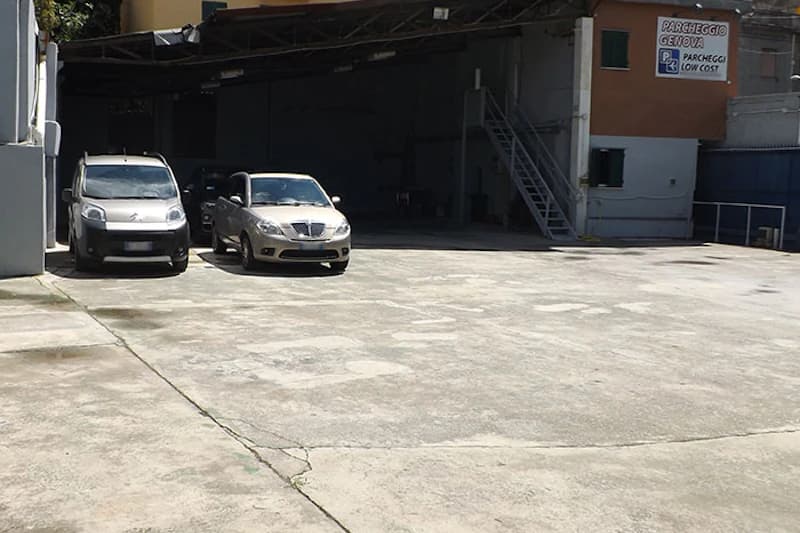 Gepflasterte Parkfläche vor offener Garage mit zwei geparkten Autos und Außentreppe am Gebäude.