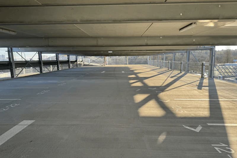 Leeres oberes Parkdeck mit markierten Parkfeldern, Stahlträgern und Sonnenlichtschatten.