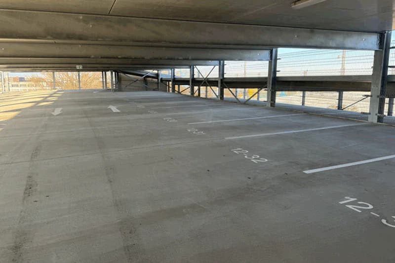 Leeres oberes Parkdeck mit nummerierten Stellflächen, Betonboden, Pfeilmarkierungen und Metallgeländer.