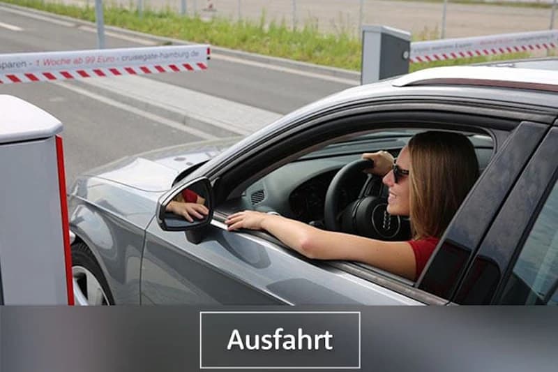 Frau im Auto mit Sonnenbrille reicht Arm zur Schranke an der Ausfahrt eines Parkplatzes.