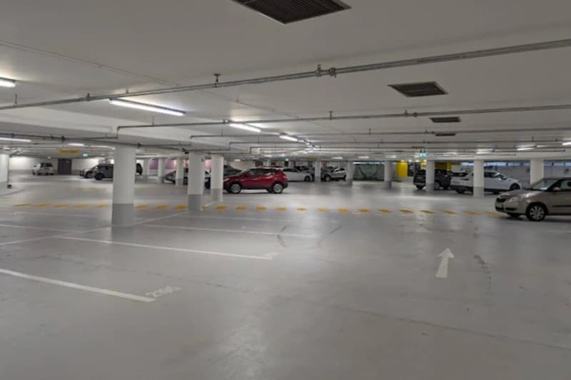 Helle Tiefgarage mit Stützpfeilern, markierten Parkplätzen, mehreren geparkten Autos und Fahrpfeil auf dem Boden.