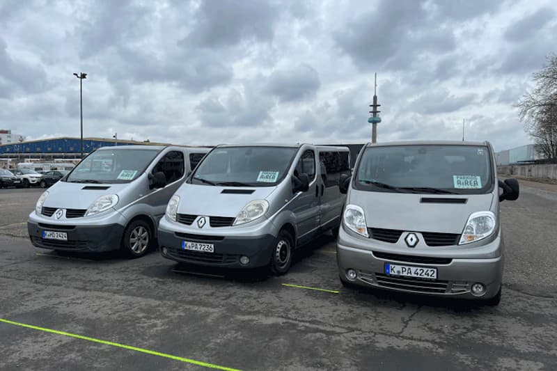Drei silberne Renault Transporter nebeneinander auf einem asphaltierten Parkplatz unter bewölktem Himmel.