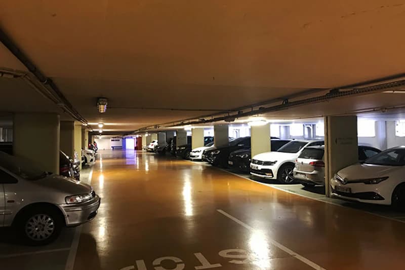 Beleuchtetes Parkdeck mit orangefarbenem Boden, Stützsäulen und geparkten Autos an beiden Seiten.