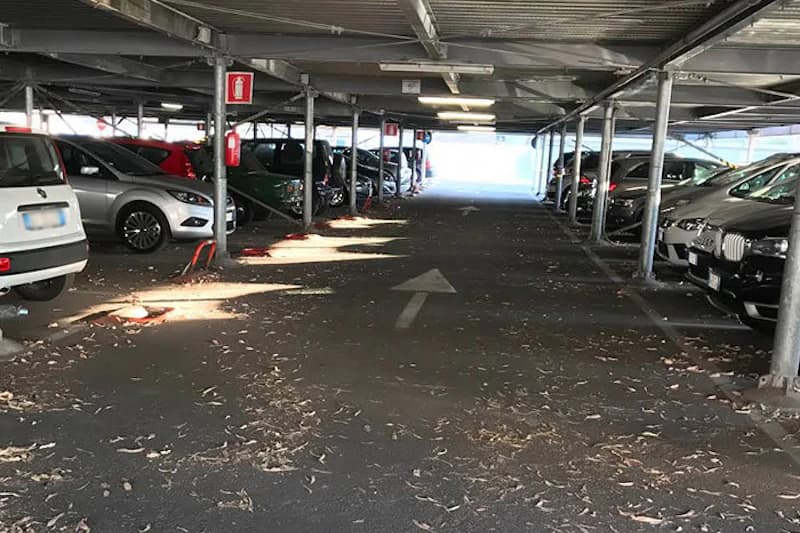 Überdachte Parkhalle mit geparkten Autos links und rechts, Mittelgang mit Richtungspfeil und verstreuten Blättern.