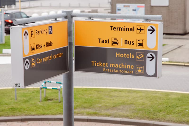 Wegweiser mit Symbolen für Parken, Flughafen, Taxi, Bus, Hotels, Ticketautomat und Mietwagen.