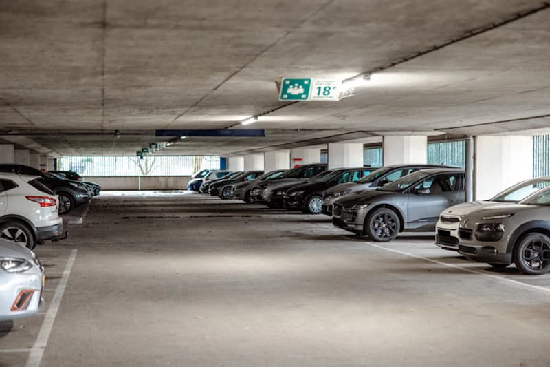 Überdachte Parkebene einer Parkgarage mit geparkten Autos, Betonstützen und Deckenleuchten.