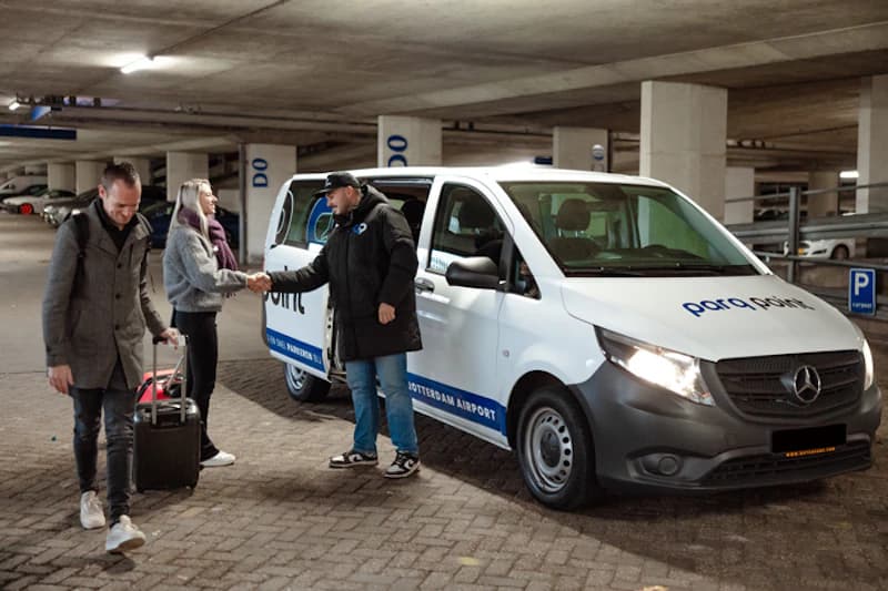 Parkhaus mit parq point Fahrzeug, Mitarbeiter schüttelt Kundin die Hand, Gepäck sichtbar.