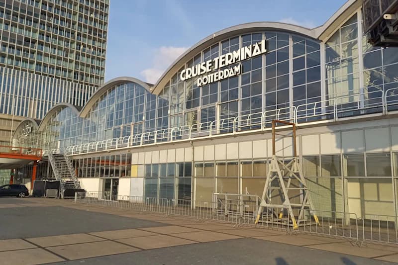 Gebäude mit geschwungener Glasfassade und Schriftzug CRUISE TERMINAL ROTTERDAM, Vorplatz mit Absperrgittern.