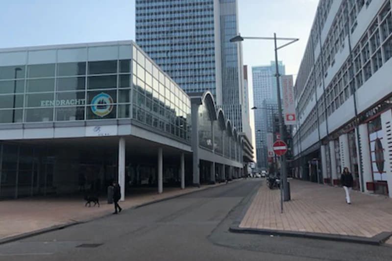 Straße zwischen modernen Bürogebäuden mit Glasfassade EENDRACHT, Laternen, zwei Fußgänger und Hund, Hochhaus im Hintergrund.
