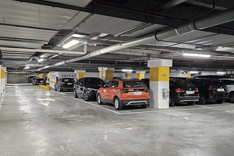 Überdachte Parkhalle mit geparkten Autos, Pfeil auf dem Boden, gelben Säulen und sichtbaren Deckenrohren.
