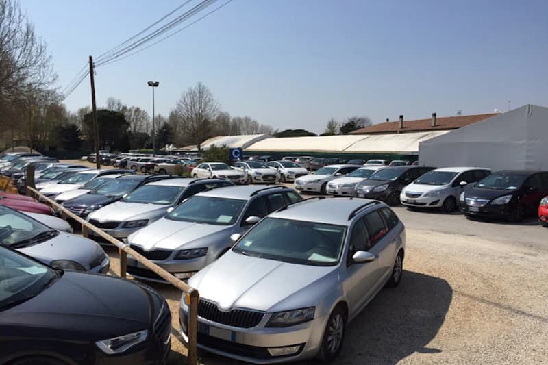 Grosser offener Parkplatz am Hafen von Venedig mit Reihen geparkter Autos, Kiesboden und Holzzaun im Vordergrund.