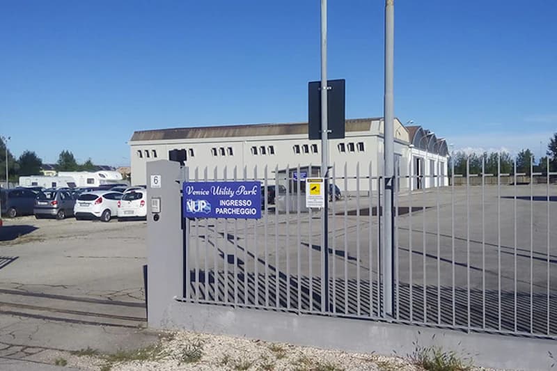 Metallzaun mit Tor, Schild Venice Utility Park Ingresso Parcheggio, geparkte Autos und Halle.